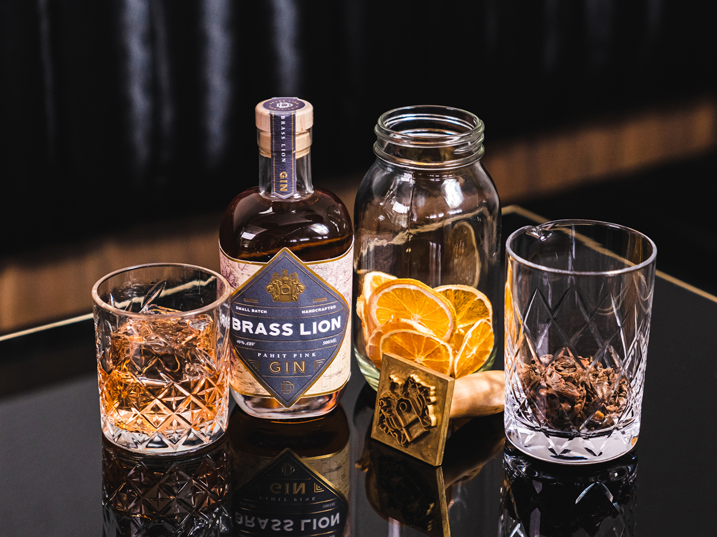 Brass Lion Pahit Pink Gin with dried spices and citrus garnishes on a reflective bar surface