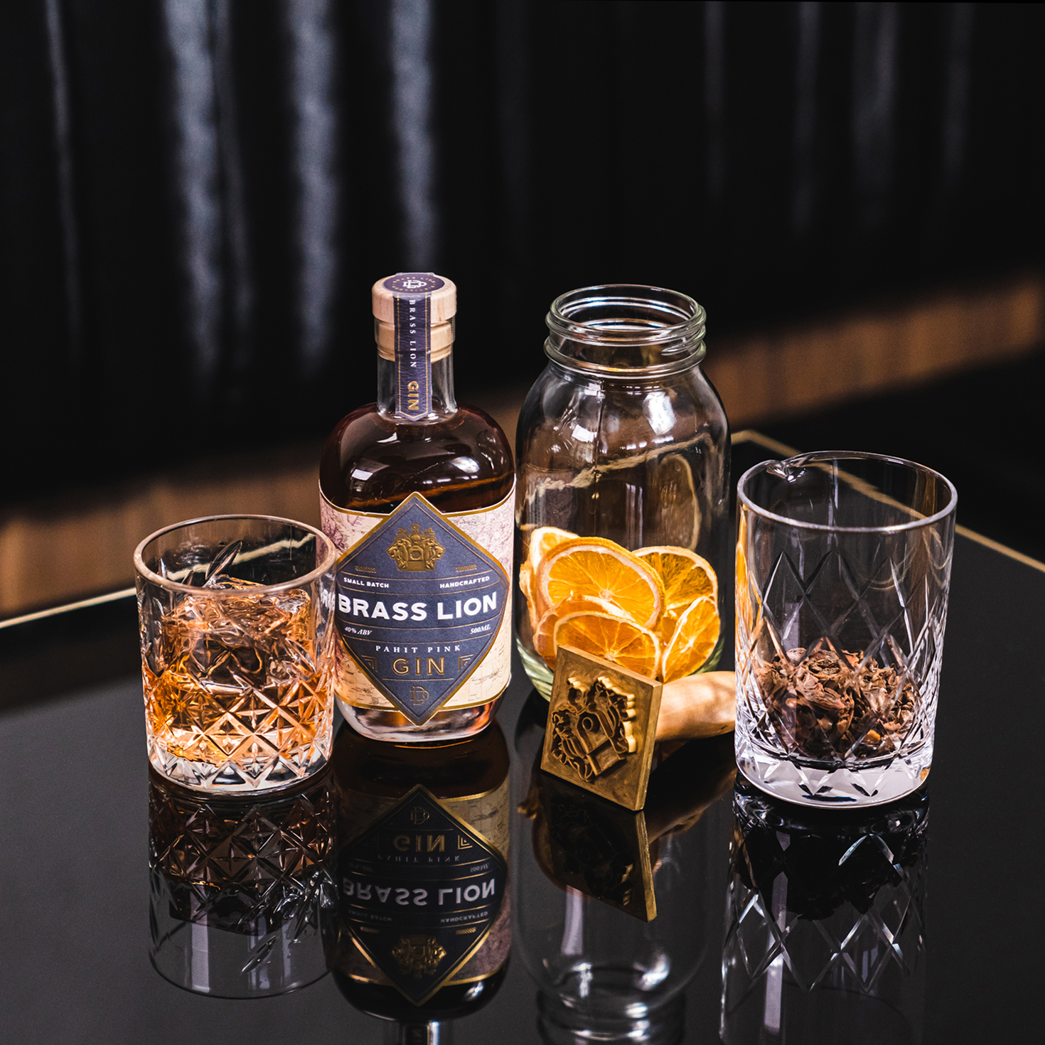 Brass Lion Pahit Pink Gin with dried spices and citrus garnishes on a reflective bar surface